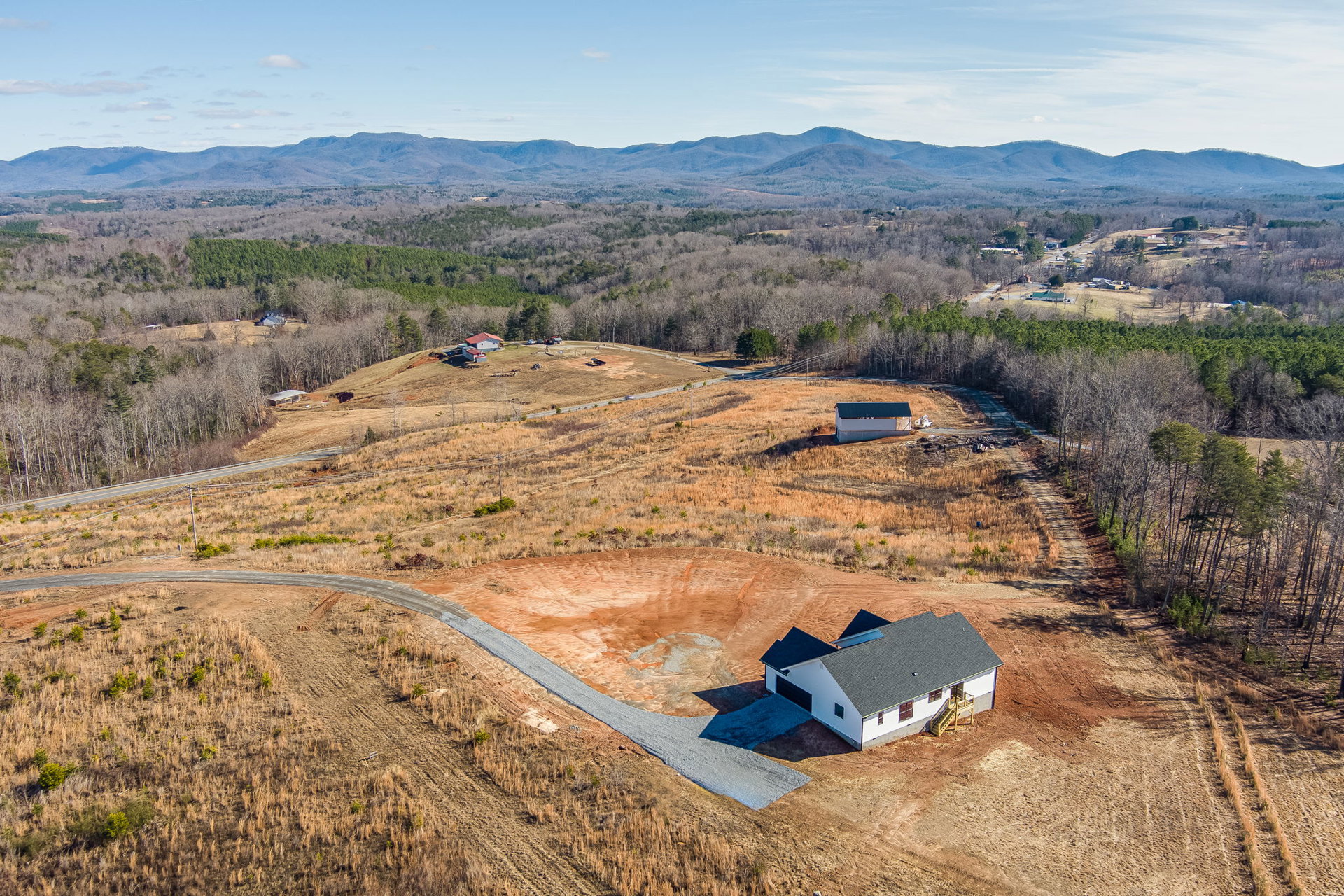 Blue and white two-story house with exterior staircase, surrounded by grassy field and hills, under a partly cloudy sky