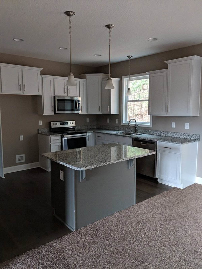 Granite island with undermount sink, stainless steel stove and microwave, white cabinetry, tile backsplash, and sunlit window in a modern kitchen