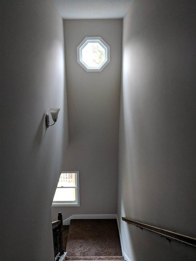 Wood staircase beneath a white hexagonal skylight, plaster walls, natural daylight streaming into modern interior.