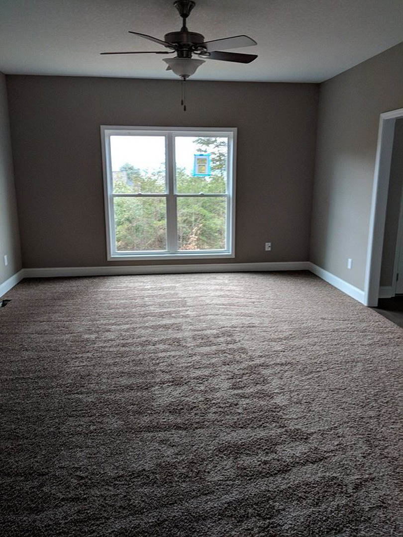 Carpeted bedroom with white walls, large window, and ceiling fan with light fixture