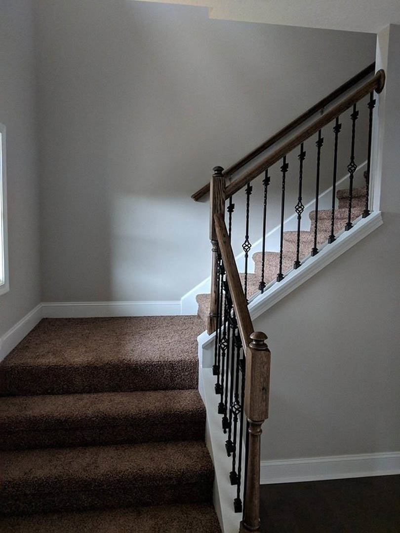 Brown carpeted staircase with black metal railing, white plaster walls, and wood trim in a residential interior.