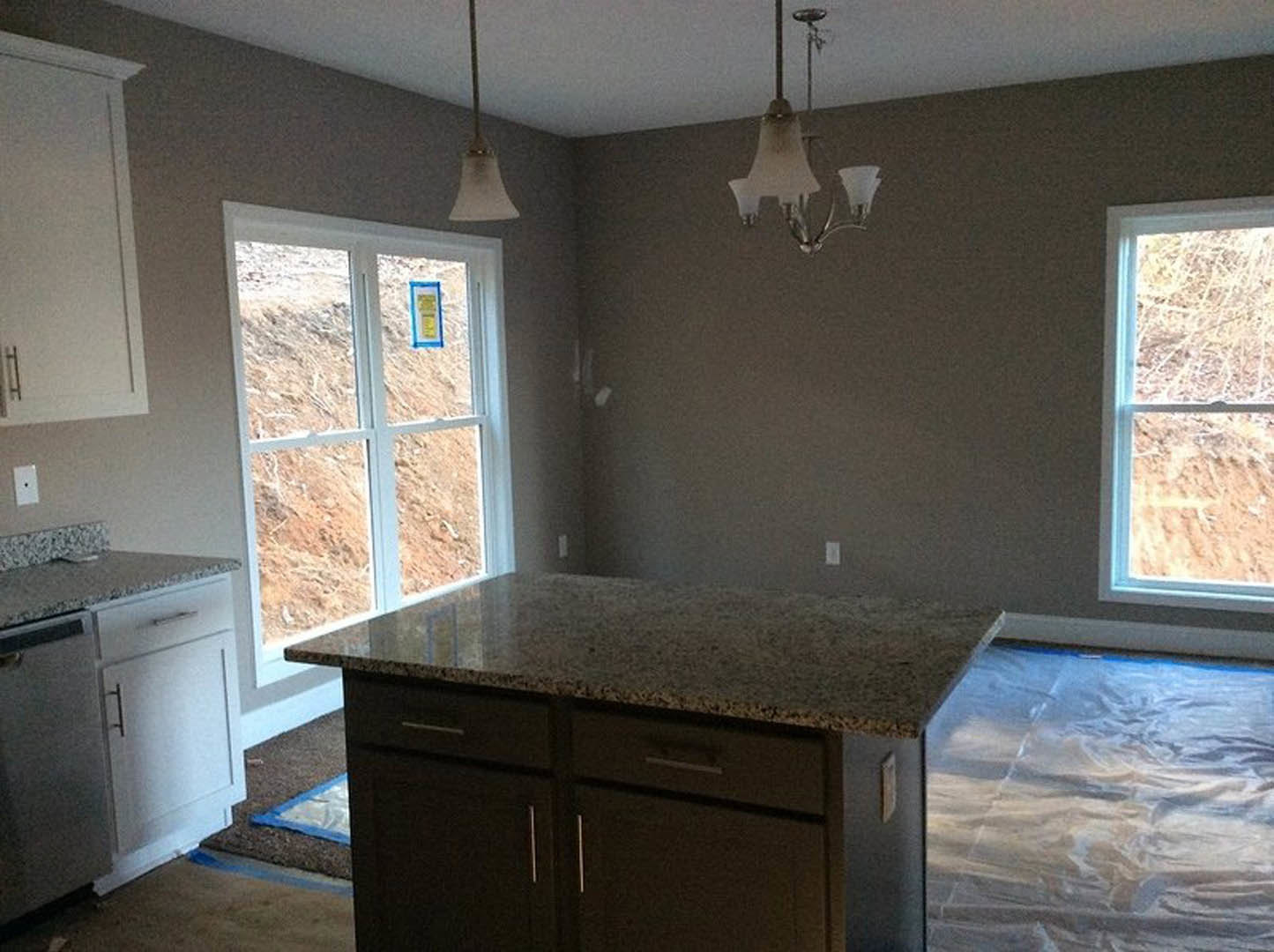 Modern kitchen featuring white cabinetry, stone countertop, stainless steel sink, and built-in appliances; plastic sheet covers the floor; large window with white frame and sign