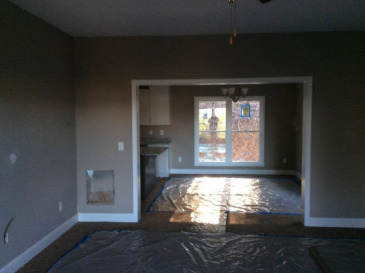 Kitchen with white walls, black countertop, stainless steel sink under a window, light wood flooring, and blue sign visible on window glass