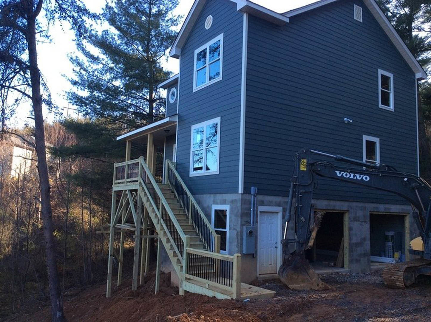 Modern house exterior with dark-framed windows reflecting trees, white door with multiple knobs, outdoor staircase, and construction crane adjacent to the building