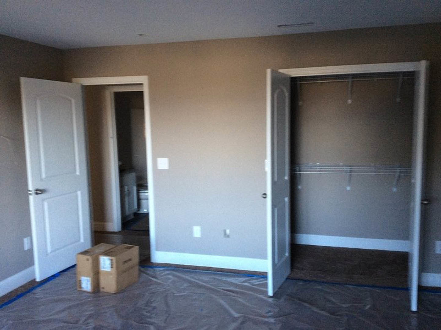 Bedroom with two white doors, a closet featuring hanging clothes, light-colored walls, and hardwood flooring