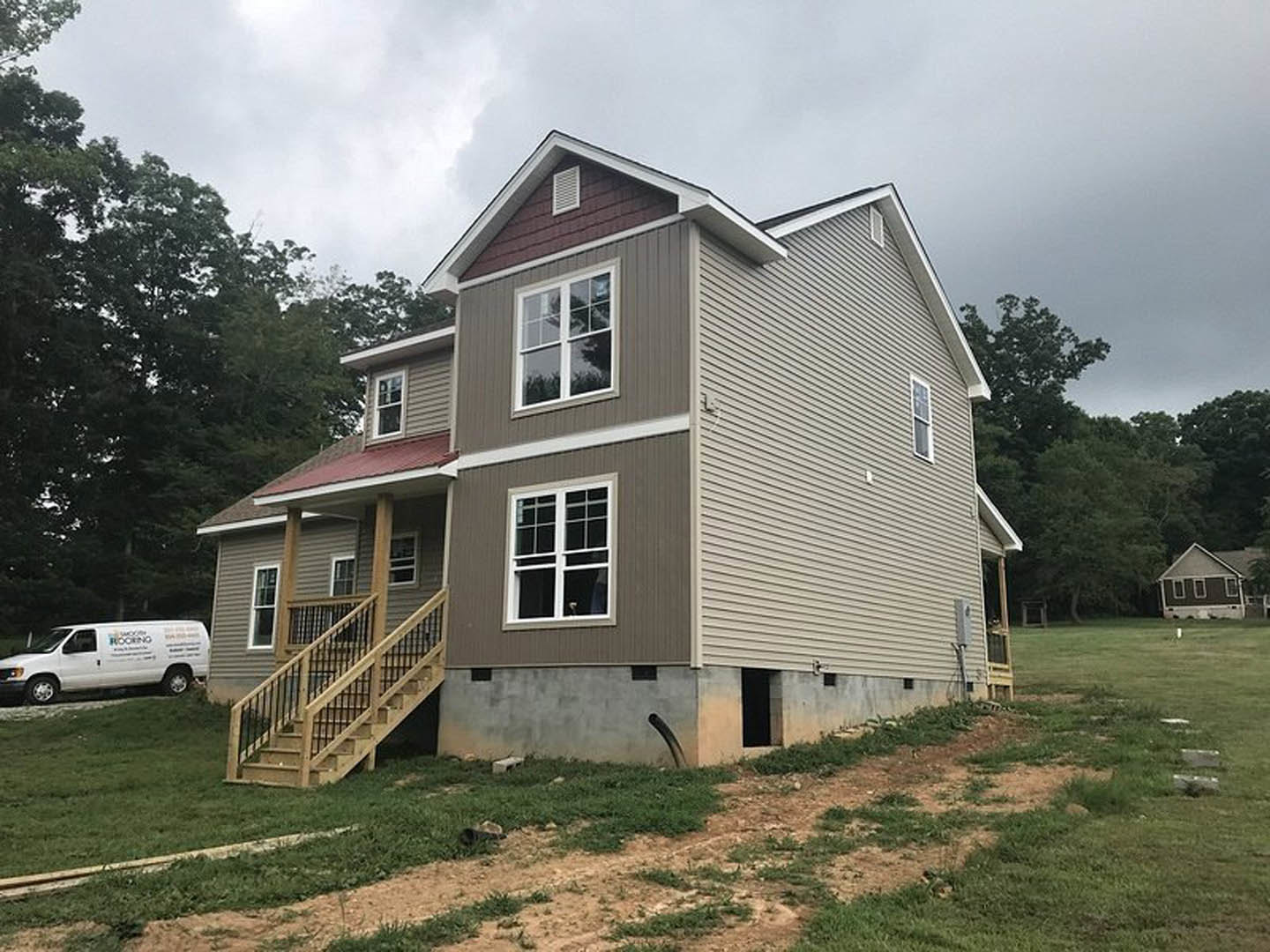 Wooden staircase with metal railing leads to covered front porch of two-story house, gray siding, large windows, landscaped lawn, white van parked nearby