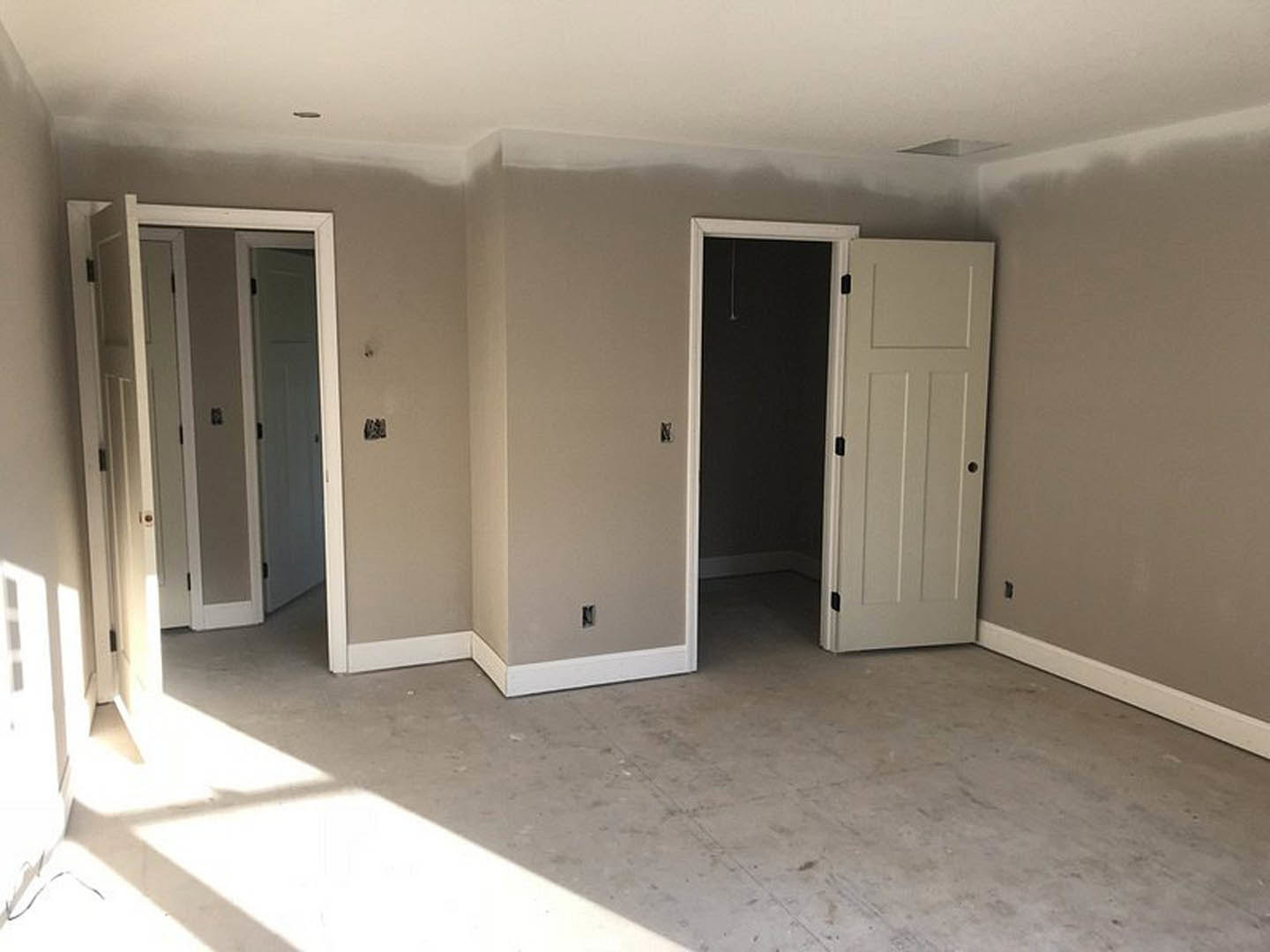 White walls and ceiling, white door with black handles, white floor and baseboard, light switch beside door