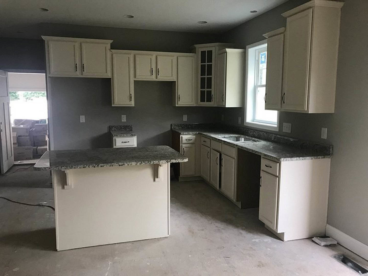 White kitchen cabinets with brushed nickel hardware, granite countertops, stainless steel sink, and a large window with a white frame above the workspace.