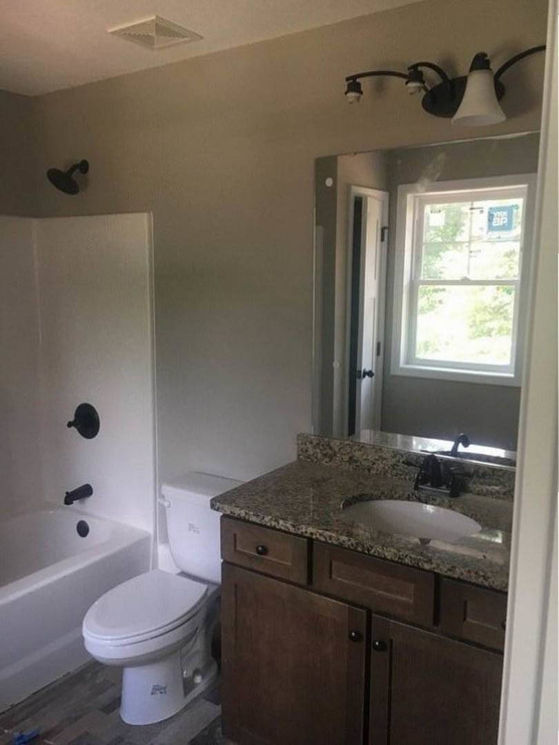 Modern bathroom featuring white porcelain sink, closed-lid toilet, freestanding bathtub, light tile flooring, wall-mounted mirror, and window with natural light.