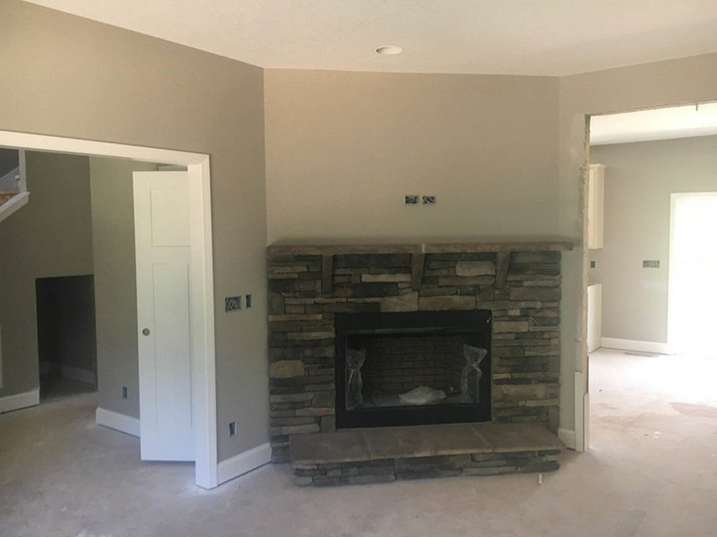 Brick fireplace with black metal frame, white plaster walls, wood flooring, white door with round knob, staircase partially visible in background