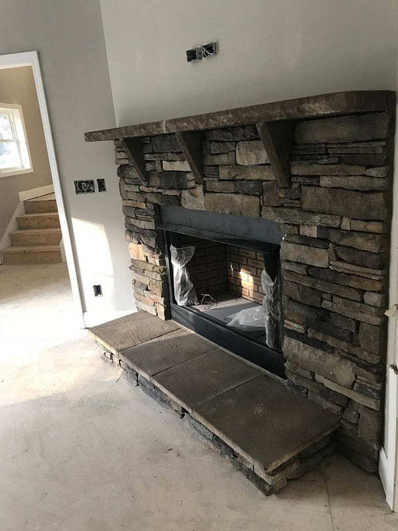 Stone fireplace with brick hearth, stone steps, and white-framed window in a room; plastic bags placed near the fireplace, close-up view of staircase.