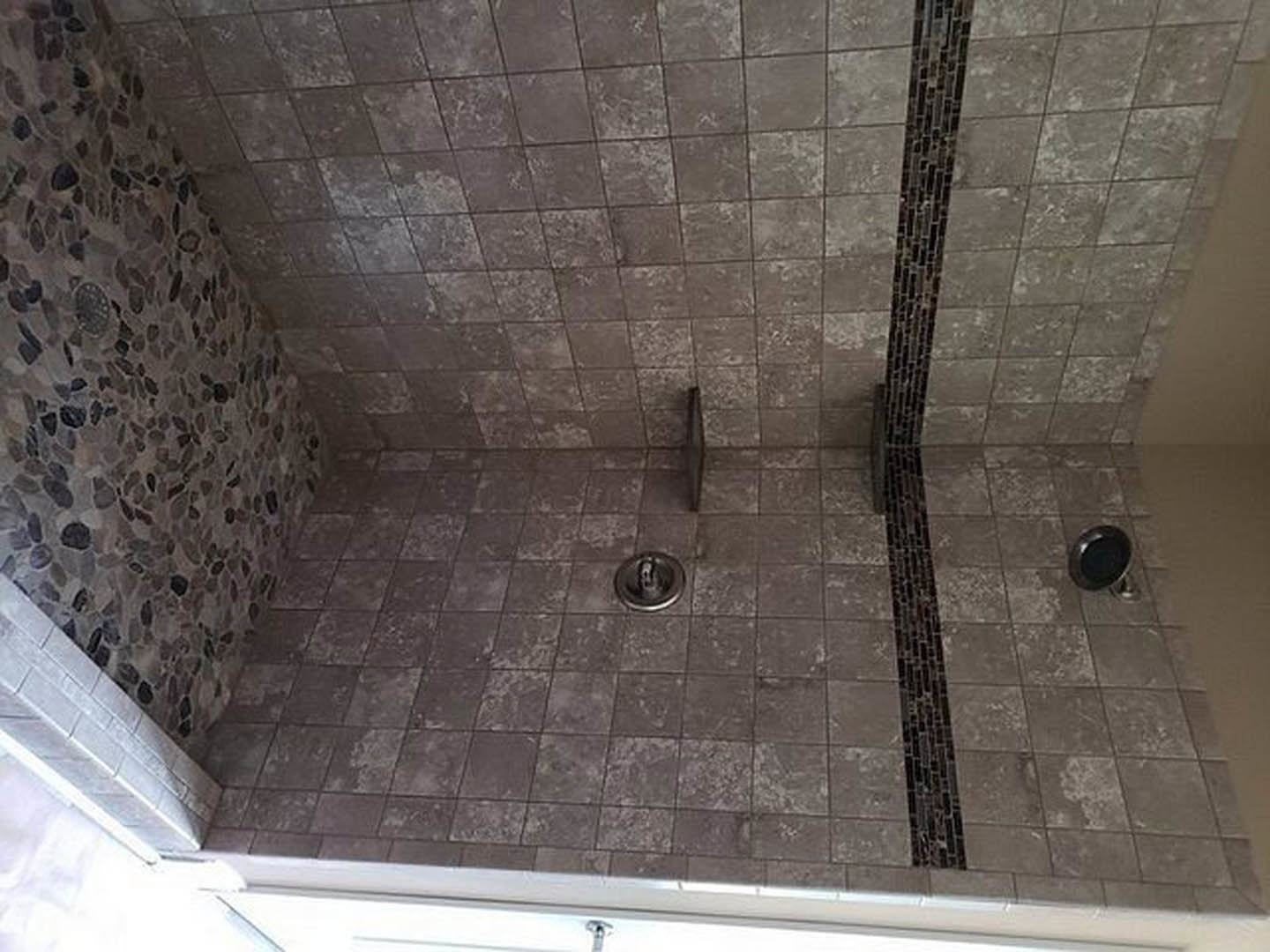 Matte black shower head mounted on light grey stone tile wall in modern bathroom