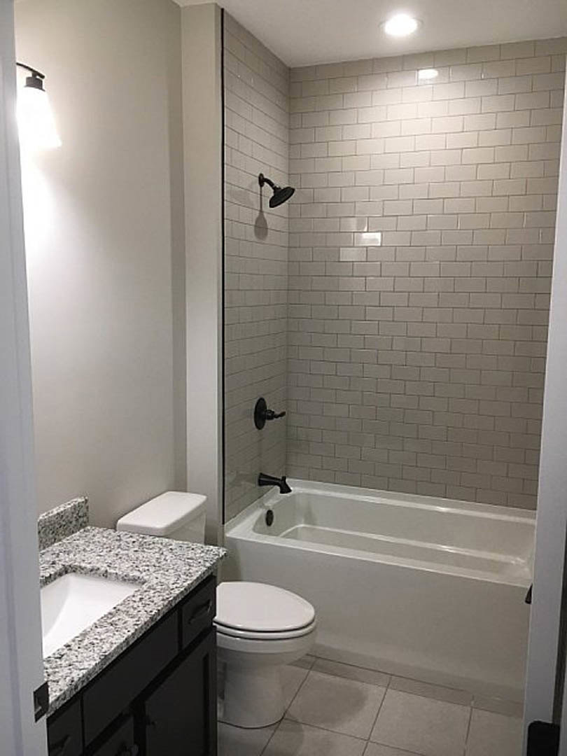 White-tiled bathroom featuring a glass-enclosed shower, freestanding soaking tub, modern vanity with vessel sink, and closed toilet; chrome fixtures and neutral wall tiles create a