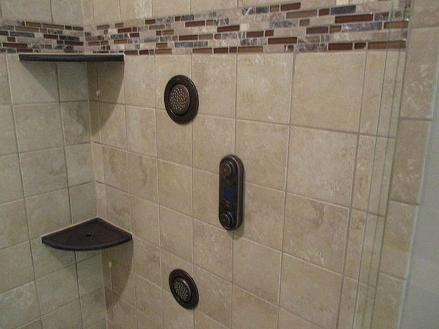 Shower with gray tile wall, built-in shelf holding toiletries, chrome drain cover visible on floor