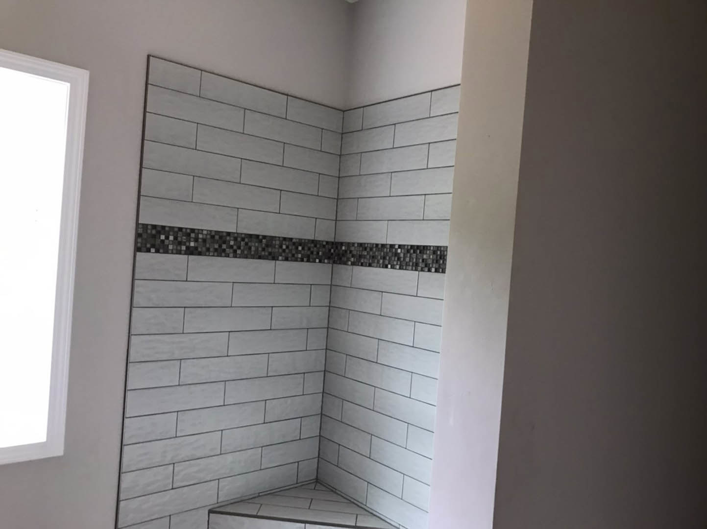 White tile shower with built-in bench and black and white tile border