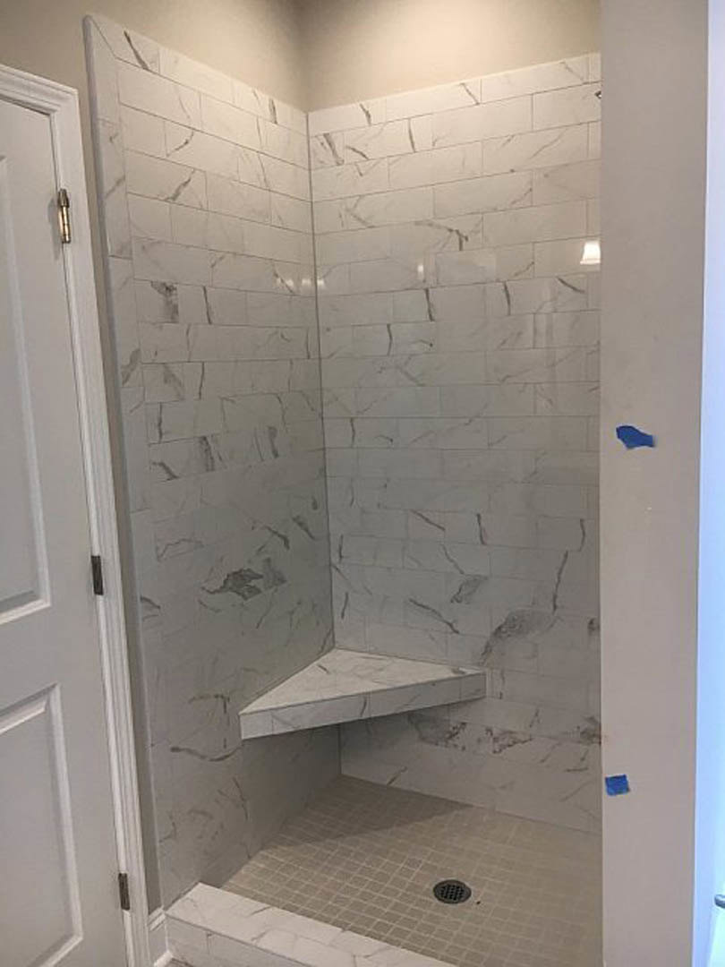 Walk-in shower with built-in bench, white tile walls, geometric patterned accent, recessed shelf, linear floor drain, and contrasting grout lines.