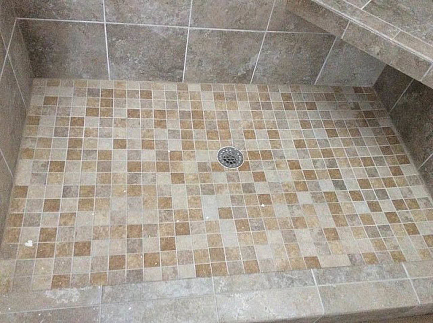 Gray tile shower floor with circular metal drain, white square accent, and stone finish