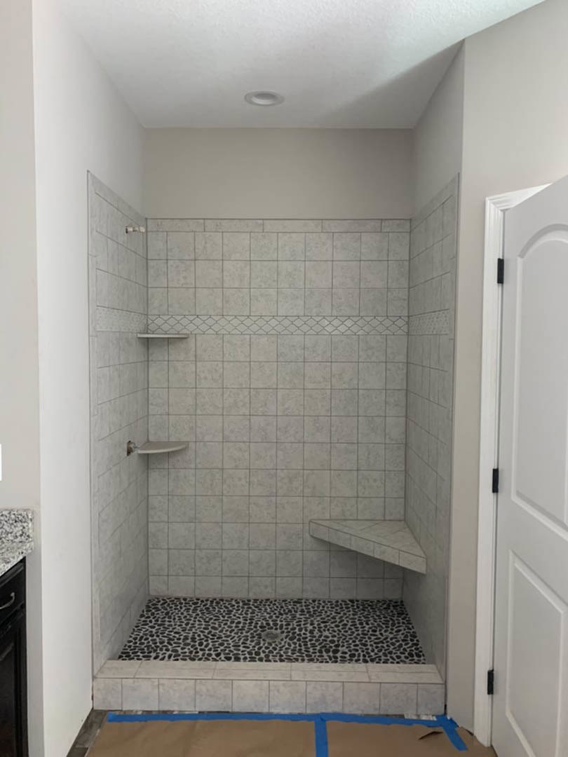 Shower with black and white speckled tile floor, white plaster walls, white door with black handle