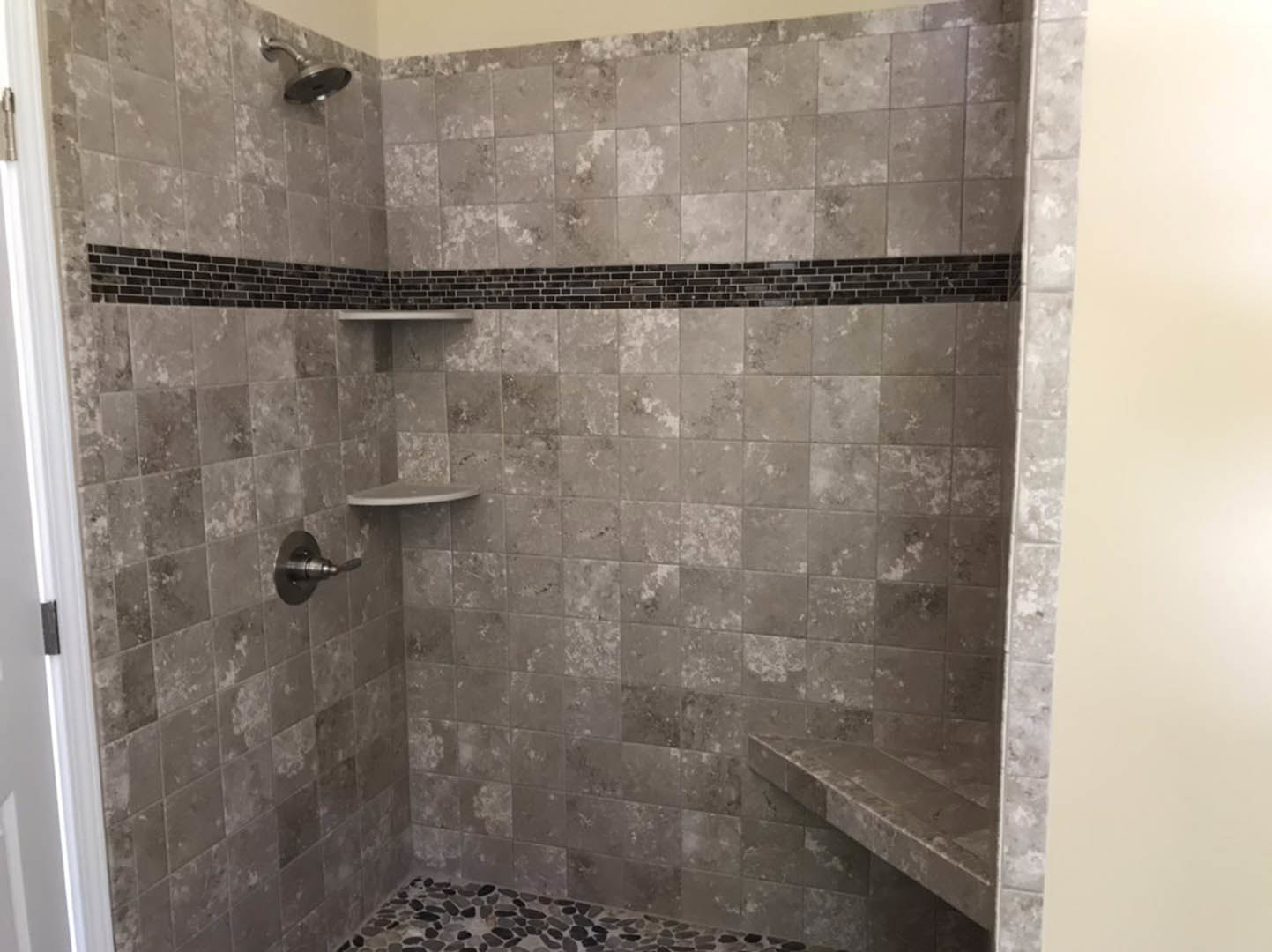 Walk-in shower with gray tile floor, marble stone shelf, chrome shower head and knob, white door frame, and plastered walls