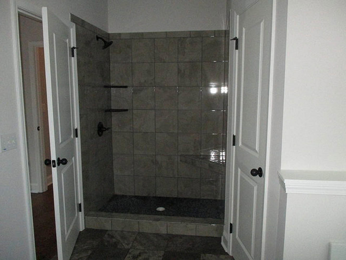 Walk-in shower featuring a patterned tile floor, tiled walls, glass door with metal handle, and modern plumbing fixtures