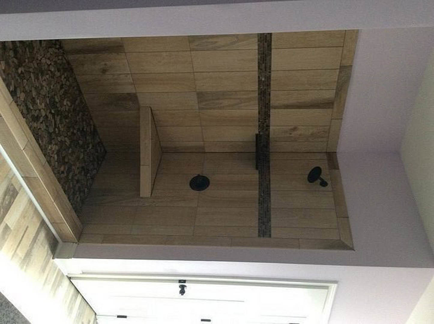 Walk-in shower with light gray tile floor, white plaster walls, and glass door; adjacent wood panel and white drawer visible.