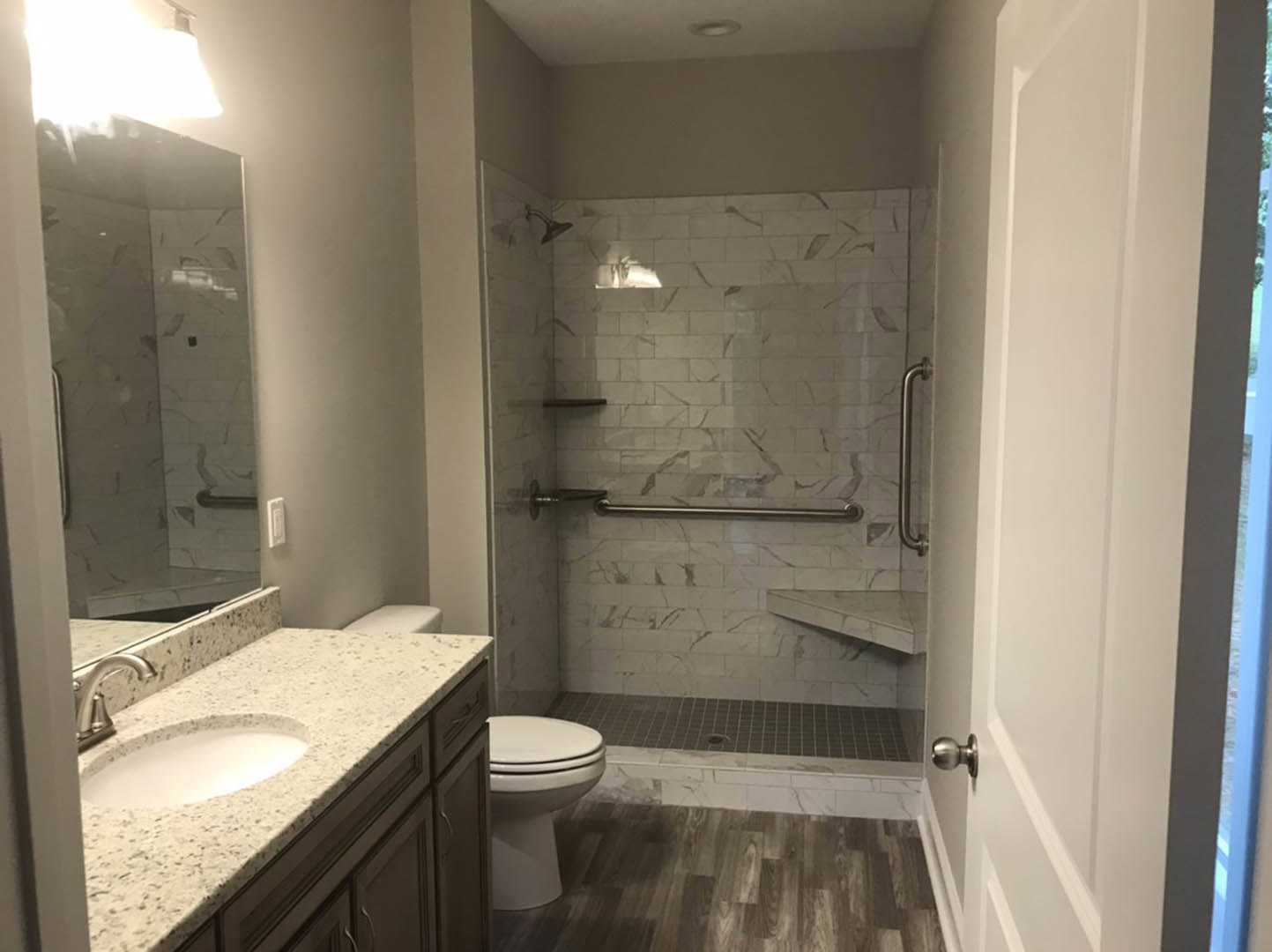 Marble-tiled shower with glass door, white marble sink with chrome faucet, wall-mounted mirror, and light-colored tile flooring