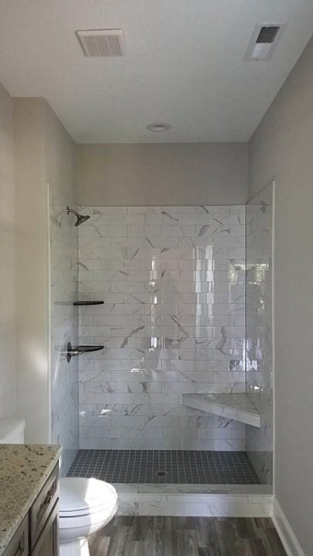 Walk-in shower featuring a tile wall, marble countertop, wood flooring, white ceiling with vent, and visible shower drain.
