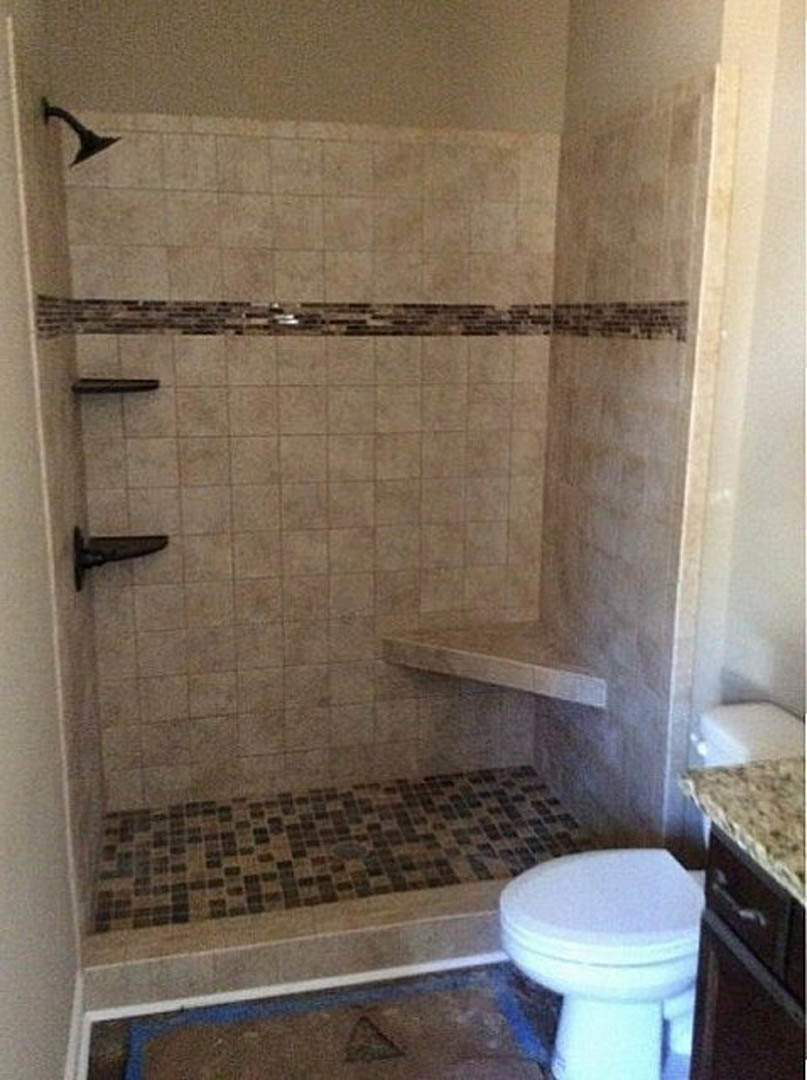 Marble-walled bathroom with glass-enclosed shower, white toilet with closed lid, and rectangular sink on a vanity