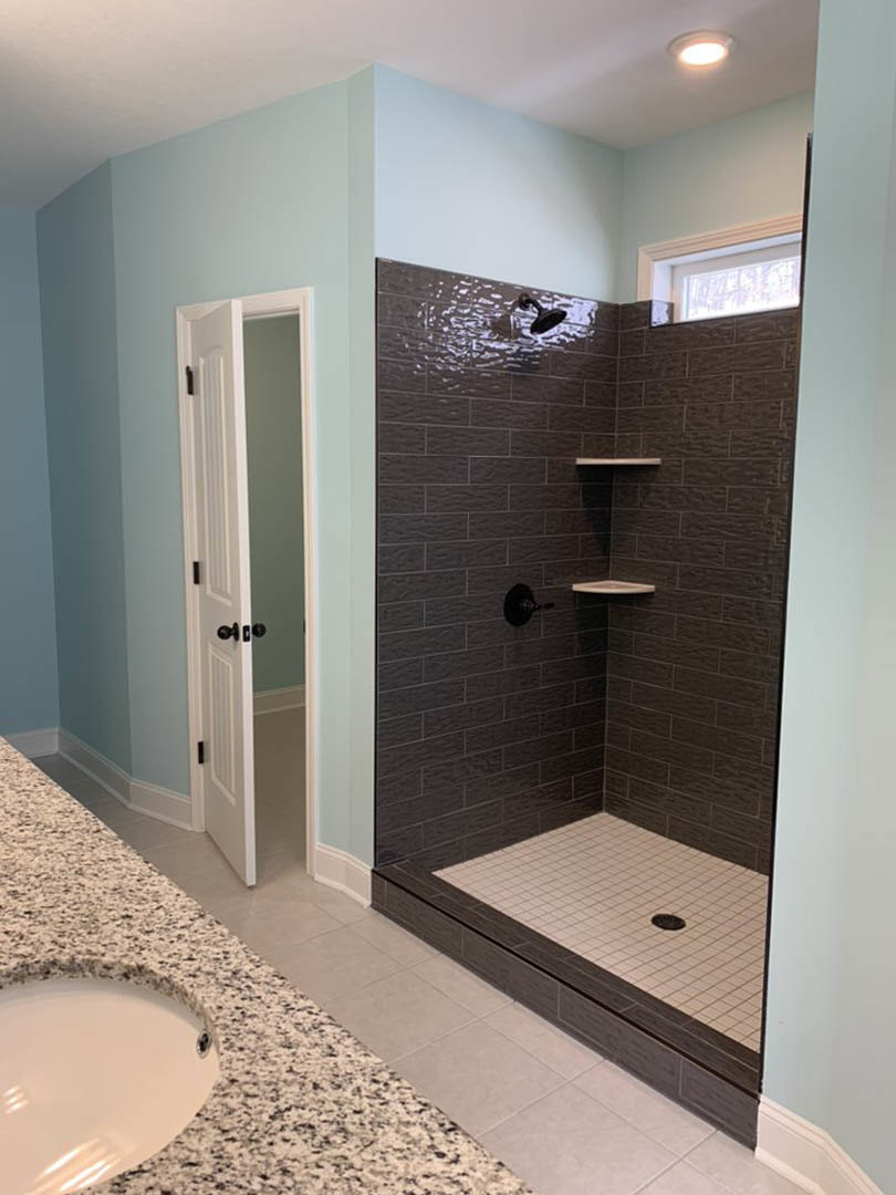 Bathroom featuring a marble countertop sink, wall-mounted mirror, glass-enclosed shower with built-in shelf, and tile flooring with central drain