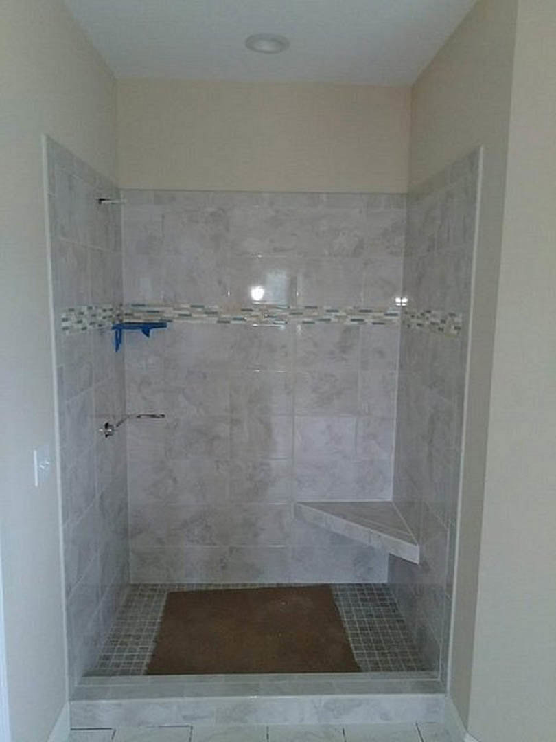 Walk-in shower with marble tile walls, brown floor mat, white tile border, and partial view of blue object in foreground