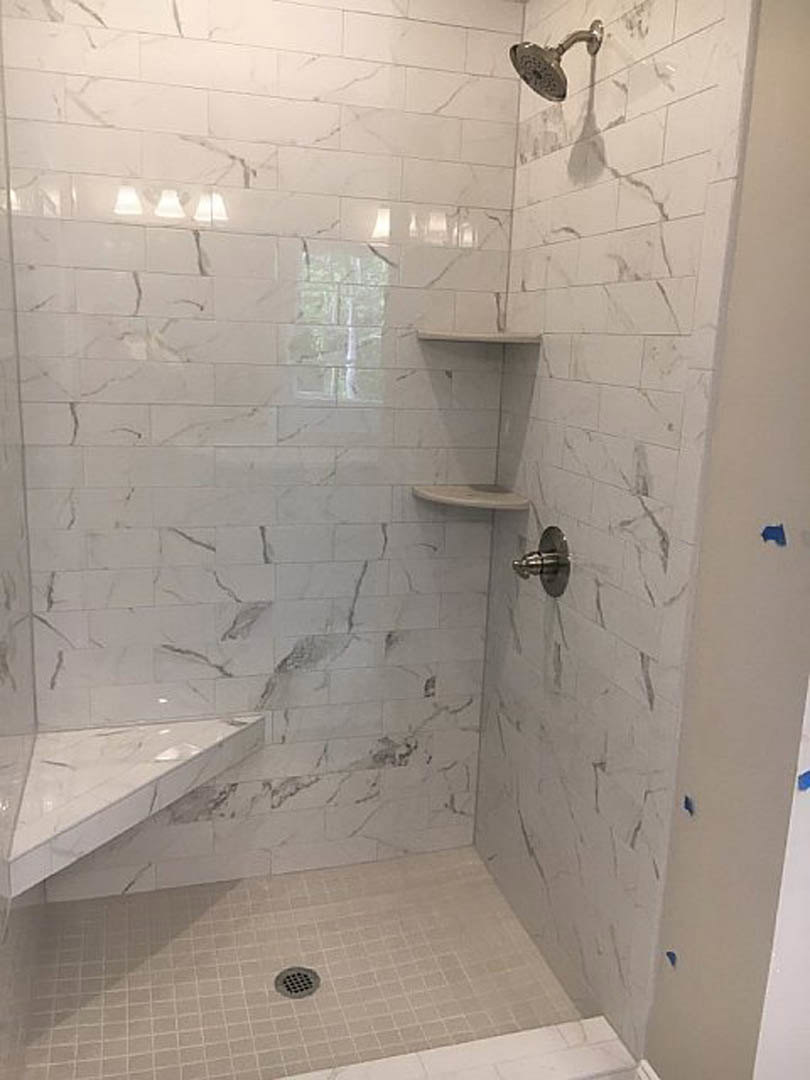 White tile shower with chrome shower head and marble corner shelf