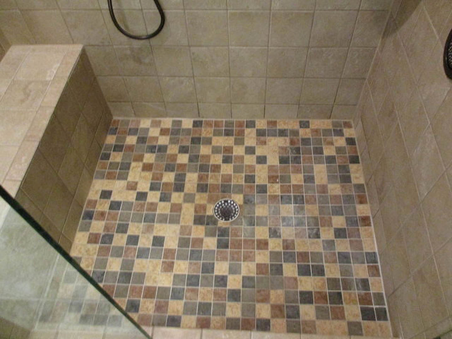 Marble-tiled shower with chrome shower head, circular drain set in tiled floor, and frameless glass enclosure