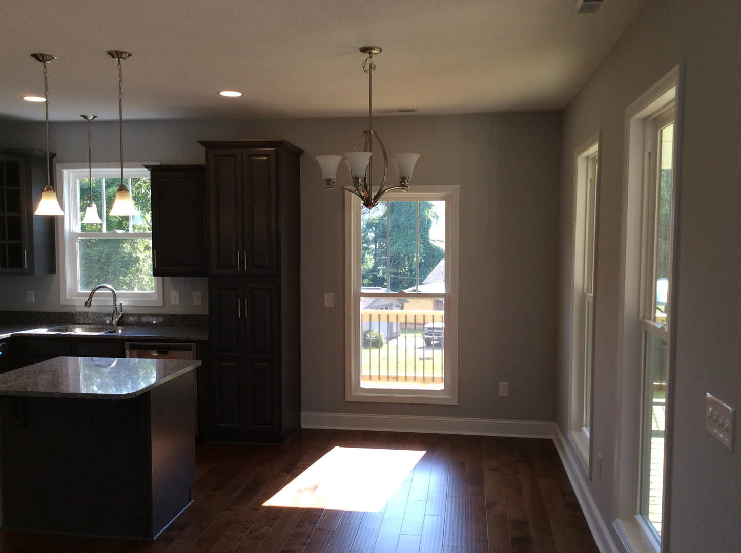 Kitchen with dark wood cabinets and silver handles, marble-topped black island, wood flooring, chandelier, window with railing overlooking trees