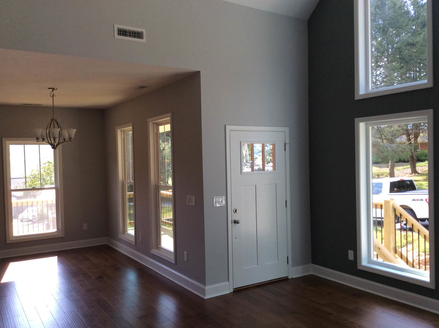 Dark wood flooring with white baseboards, white door, two windows showing trees and a white truck parked outside