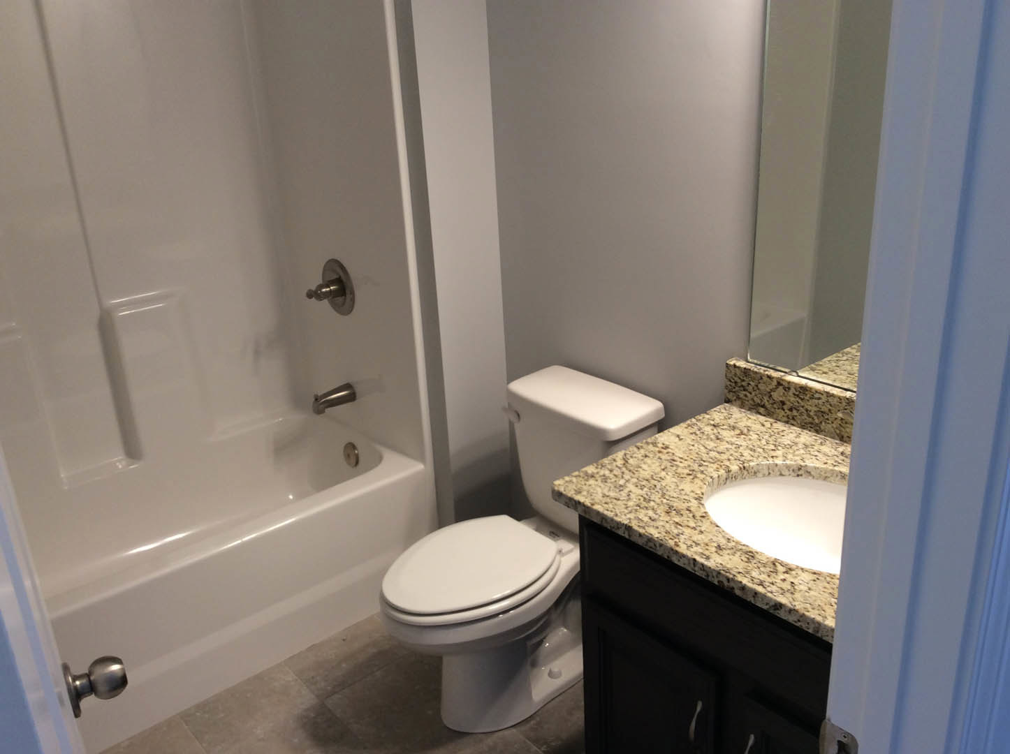 Bathroom with white porcelain sink, chrome faucet, marble countertop, wall-mounted mirror, and adjacent toilet on light tile flooring