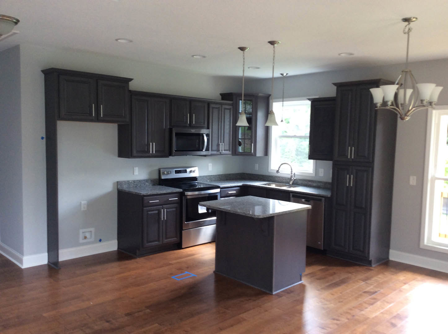 Kitchen with dark wood cabinets, marble island countertop, stainless steel oven and microwave, light-colored flooring, and modern lighting fixtures