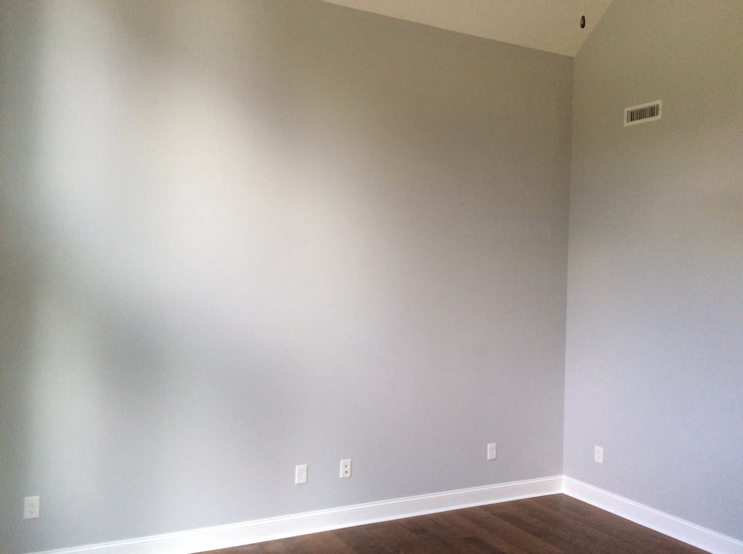 White walls with a ceiling vent, wood laminate flooring, and white baseboards in a residential room.