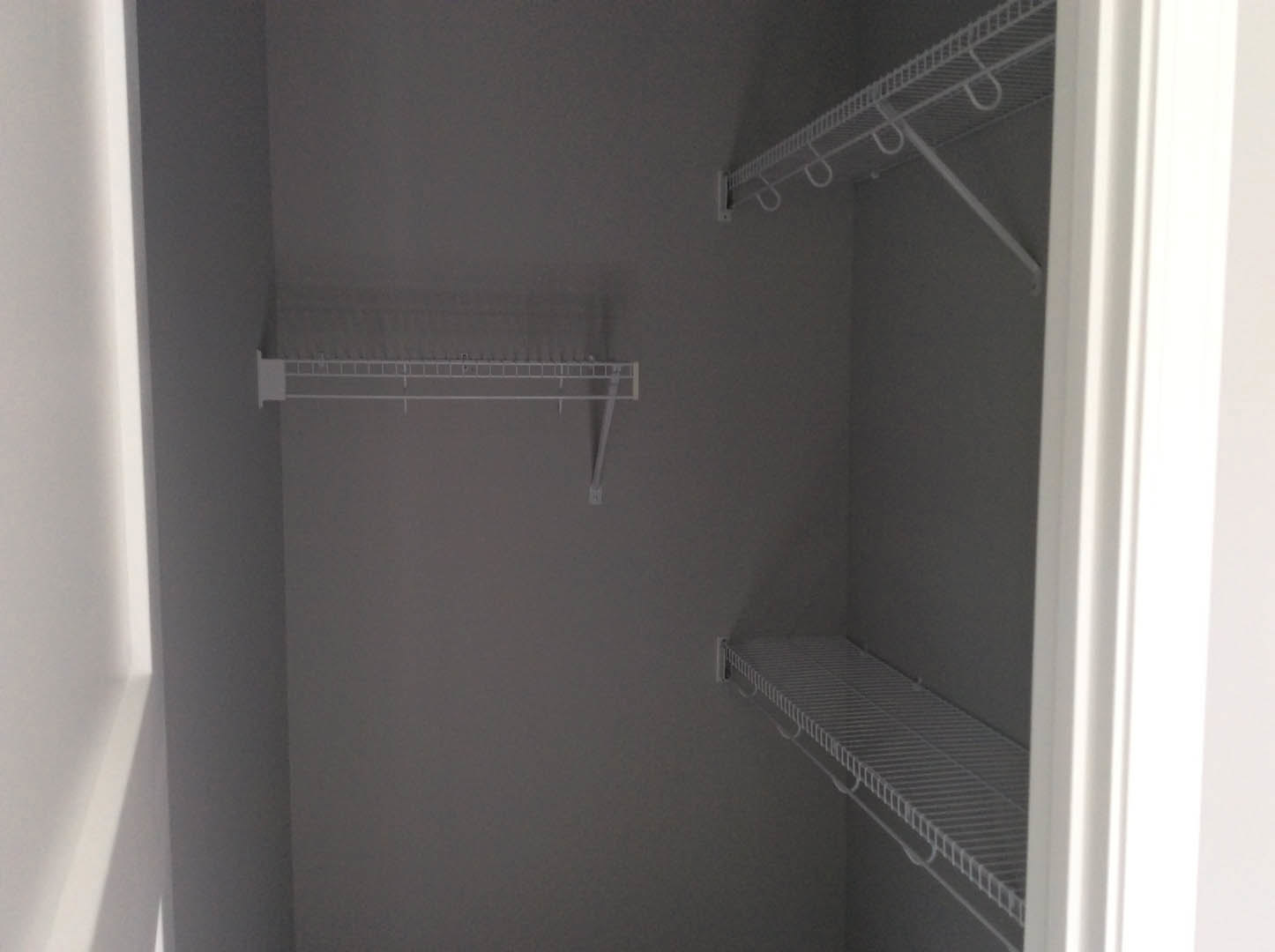 White wire shelving with integrated hooks installed in a plaster-walled closet, adjacent to a door handle and shower area.