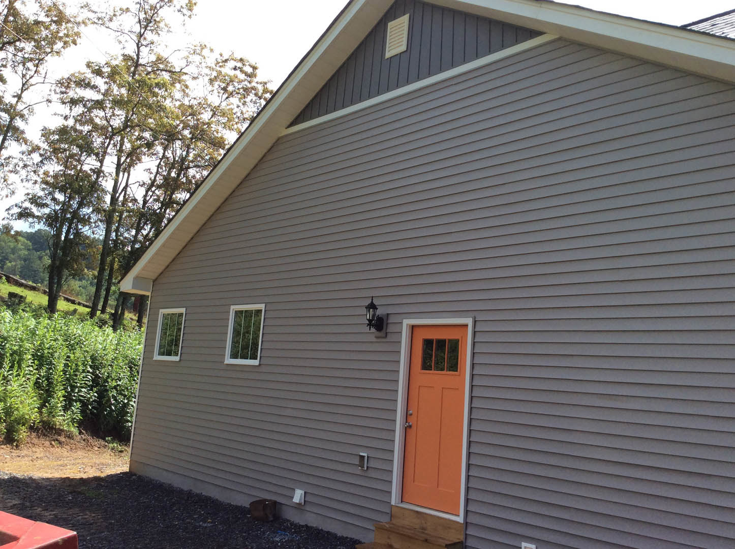 Modern home exterior with orange front door, white siding, white-framed window, garden plants, and wall vent