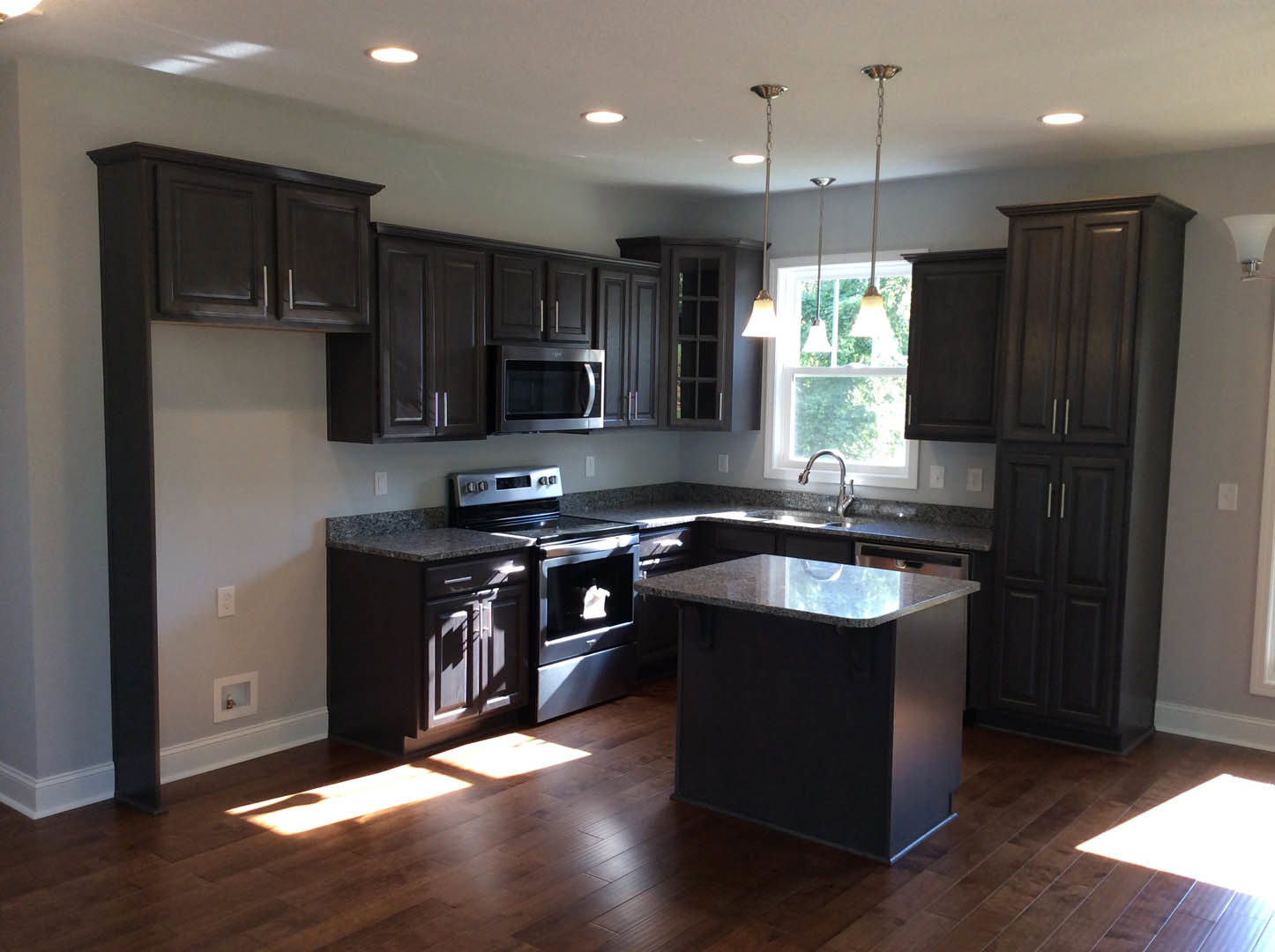 Kitchen with dark wood cabinets, marble island countertop, stainless steel microwave and oven, light walls, and hardwood flooring
