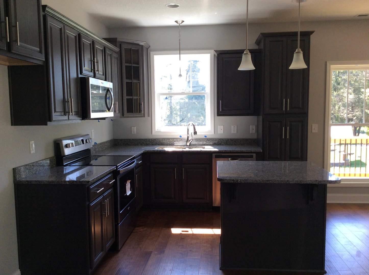 Kitchen with dark wood cabinets, black countertop, stainless steel faucet, built-in microwave, and a window letting in natural light