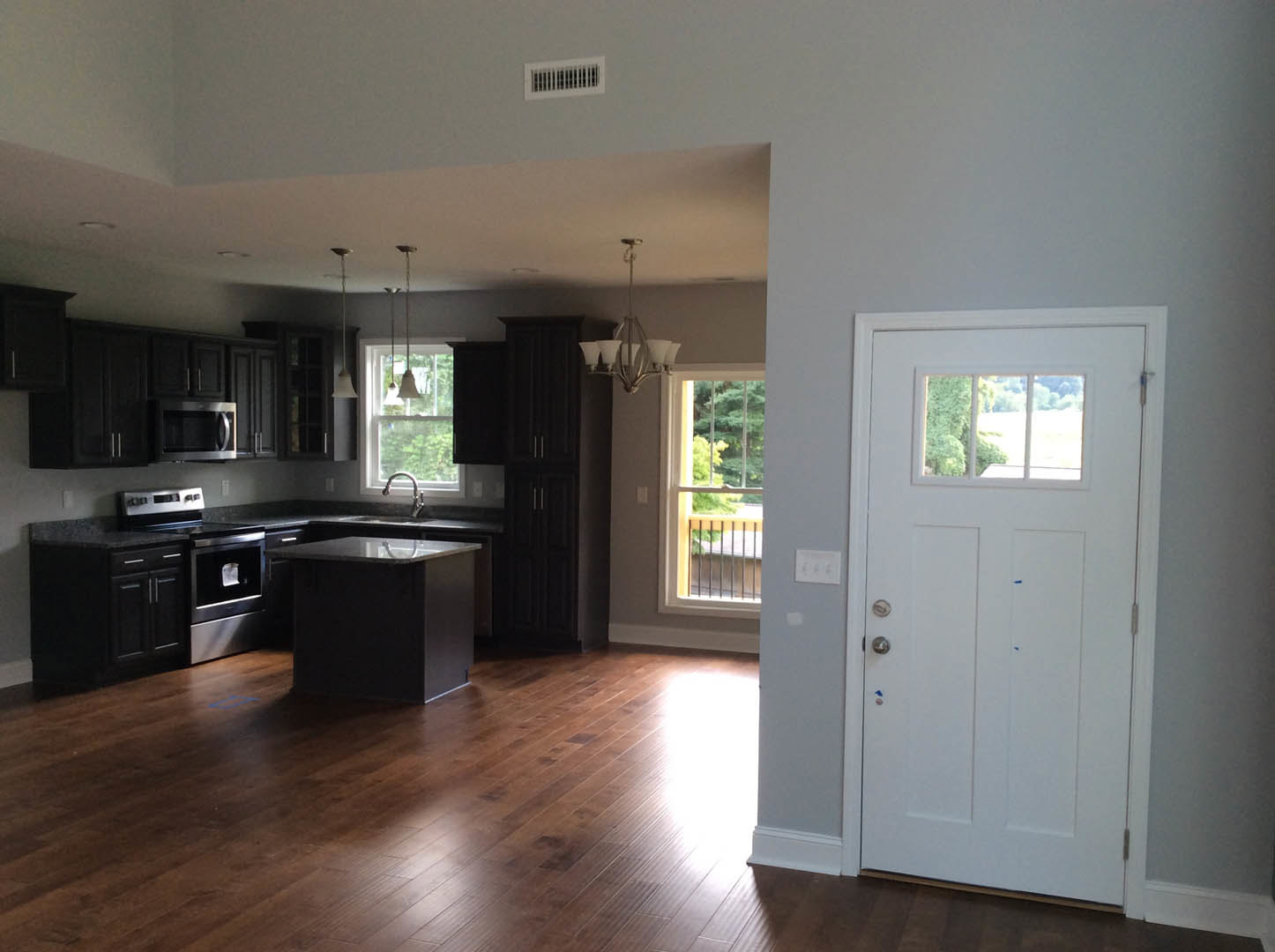 Open kitchen and dining area featuring wood flooring, white cabinetry, stainless steel appliances, a glass-topped black dining table, white door with window, wall vent, and large