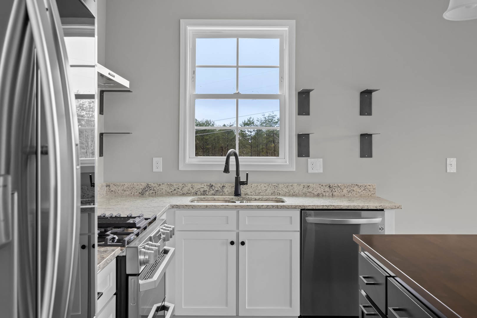 Bright kitchen with white cabinetry, stainless steel refrigerator, undermount sink beneath a window overlooking trees and blue sky, quartz countertops, chrome faucet, and modern