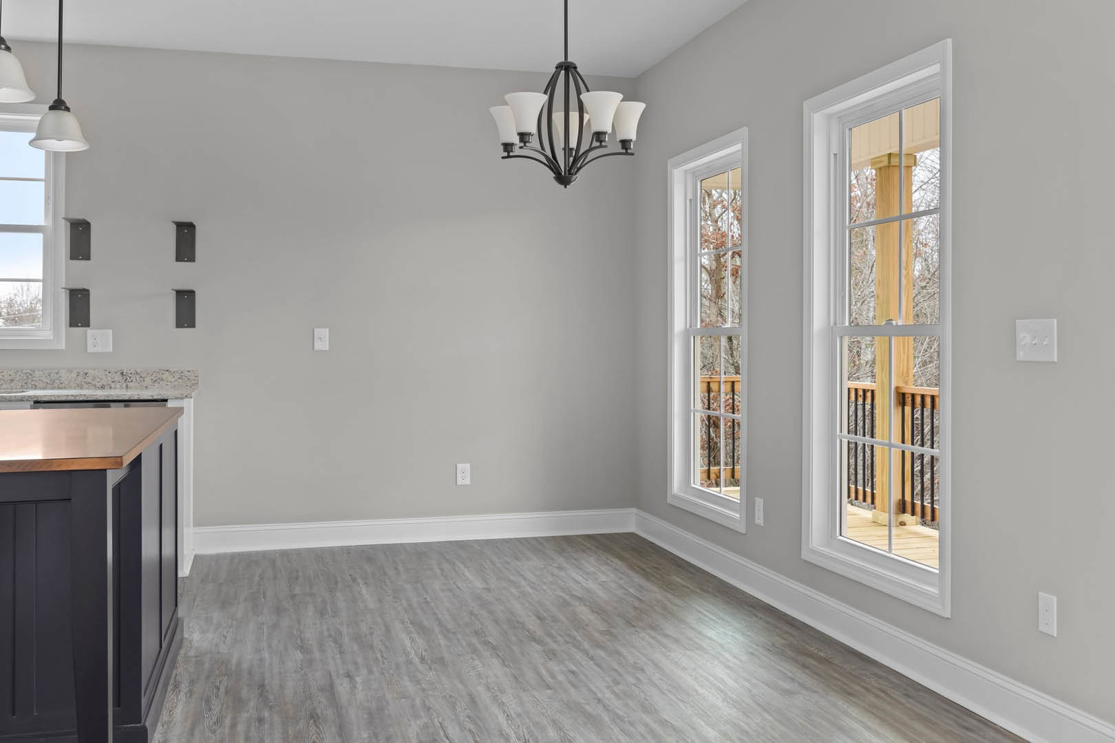 Chandelier with white shades hanging in a room featuring wood flooring, white trim, large windows with wooden railings, and a wall-mounted thermostat