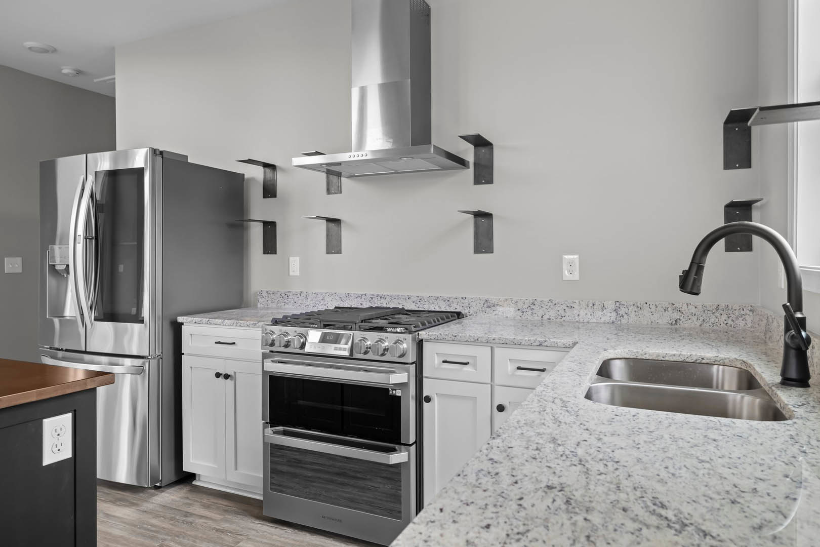 White cabinetry and appliances in a kitchen with stainless steel refrigerator, open oven door, marble countertops, black faucet, and built-in microwave