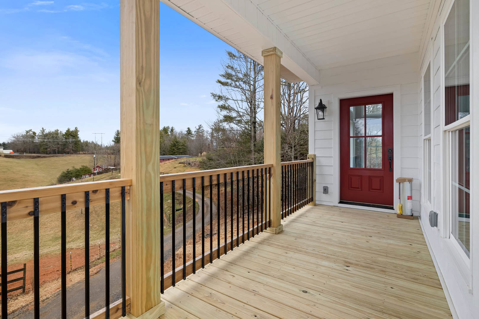Red front door framed by white pillars, black metal railing, wooden porch deck, and windows on a residential exterior