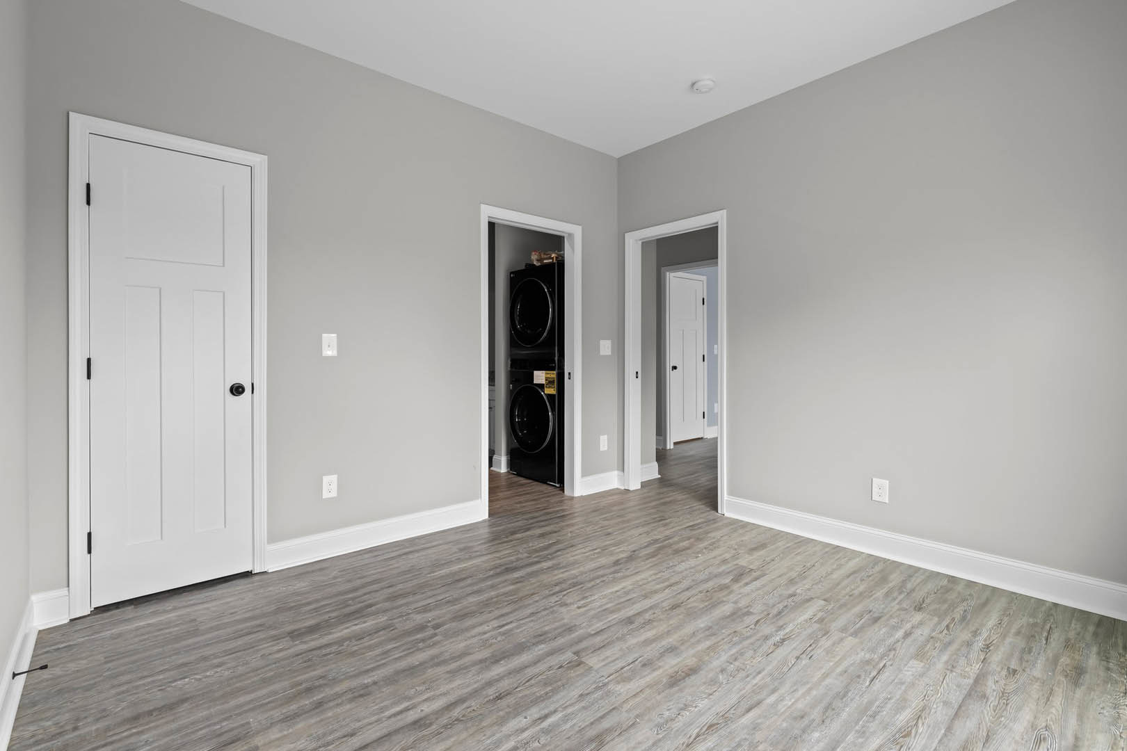 Hardwood floor with white baseboards, white paneled doors featuring black handles, washer and dryer set against a neutral wall