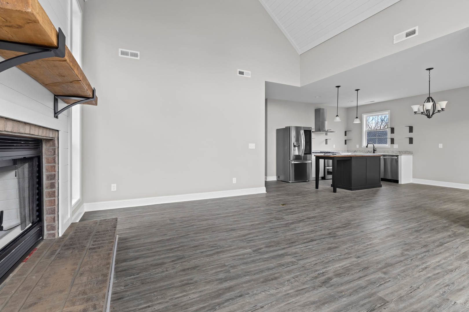 Open kitchen with white cabinetry, stainless steel refrigerator, wood flooring, dining table, large window showing blue sky, and chandelier with white shades