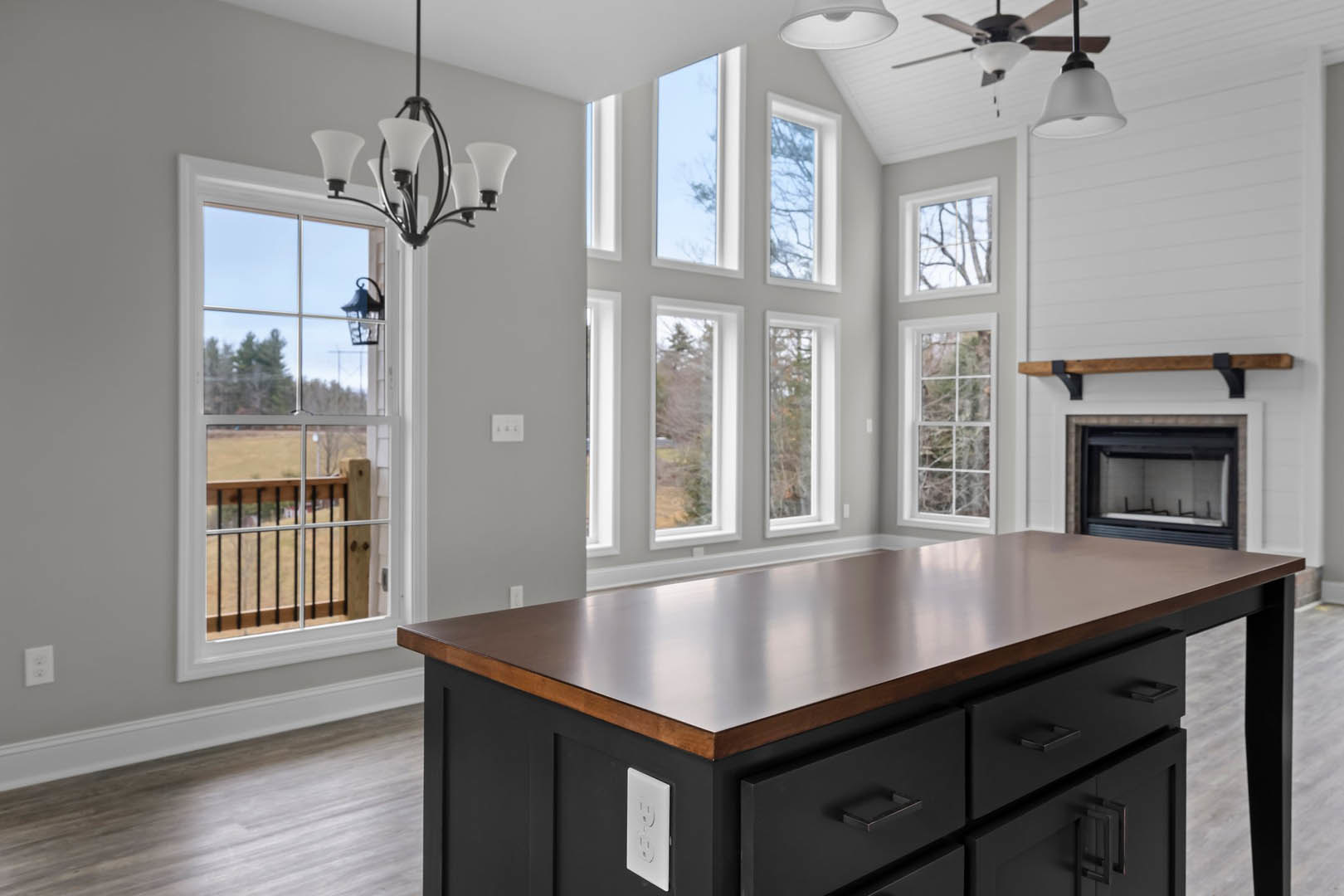 Quartz kitchen island with wood cabinetry, built-in drawers, white wall with electrical outlet and switches, glass fireplace, large window, and decorative white object with smiley