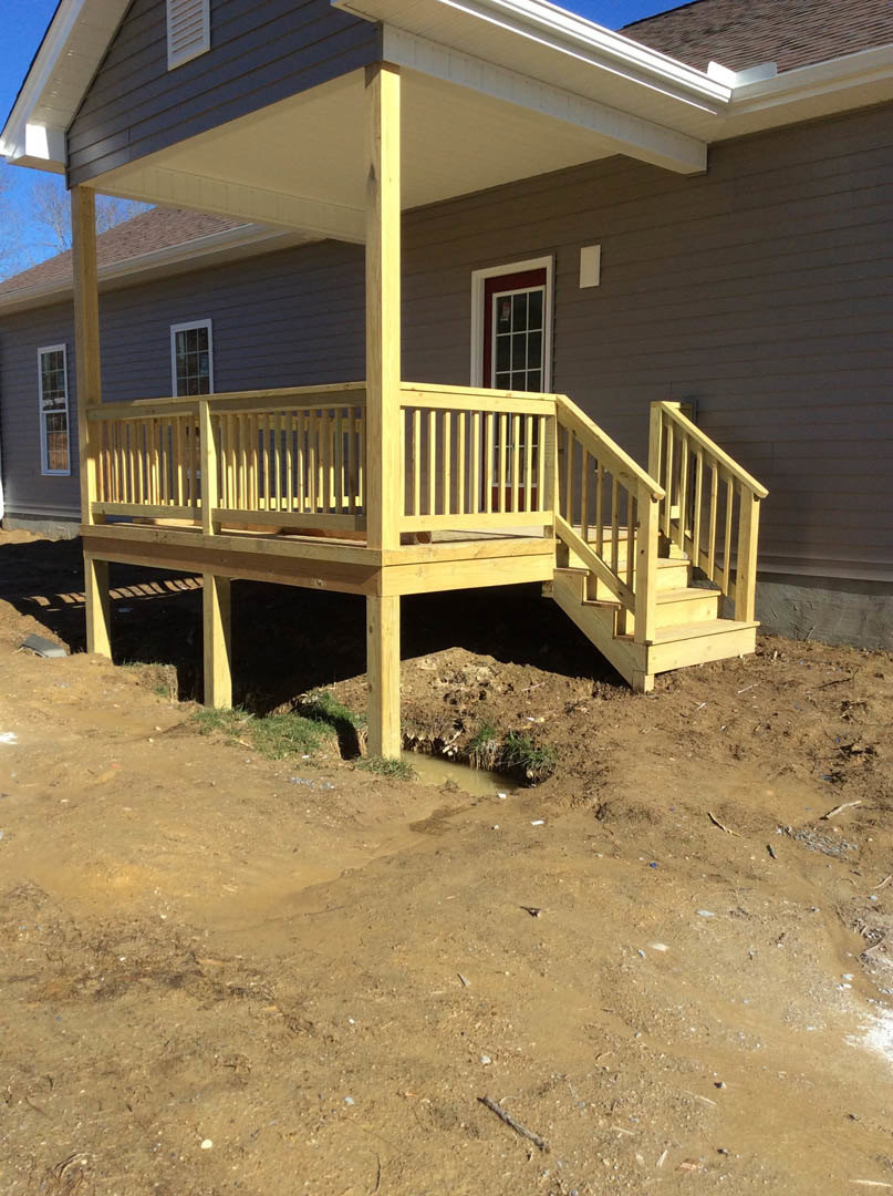 Wooden deck with railing and stairs leading to covered porch, white siding, red-trimmed window, and white vent on exterior of house